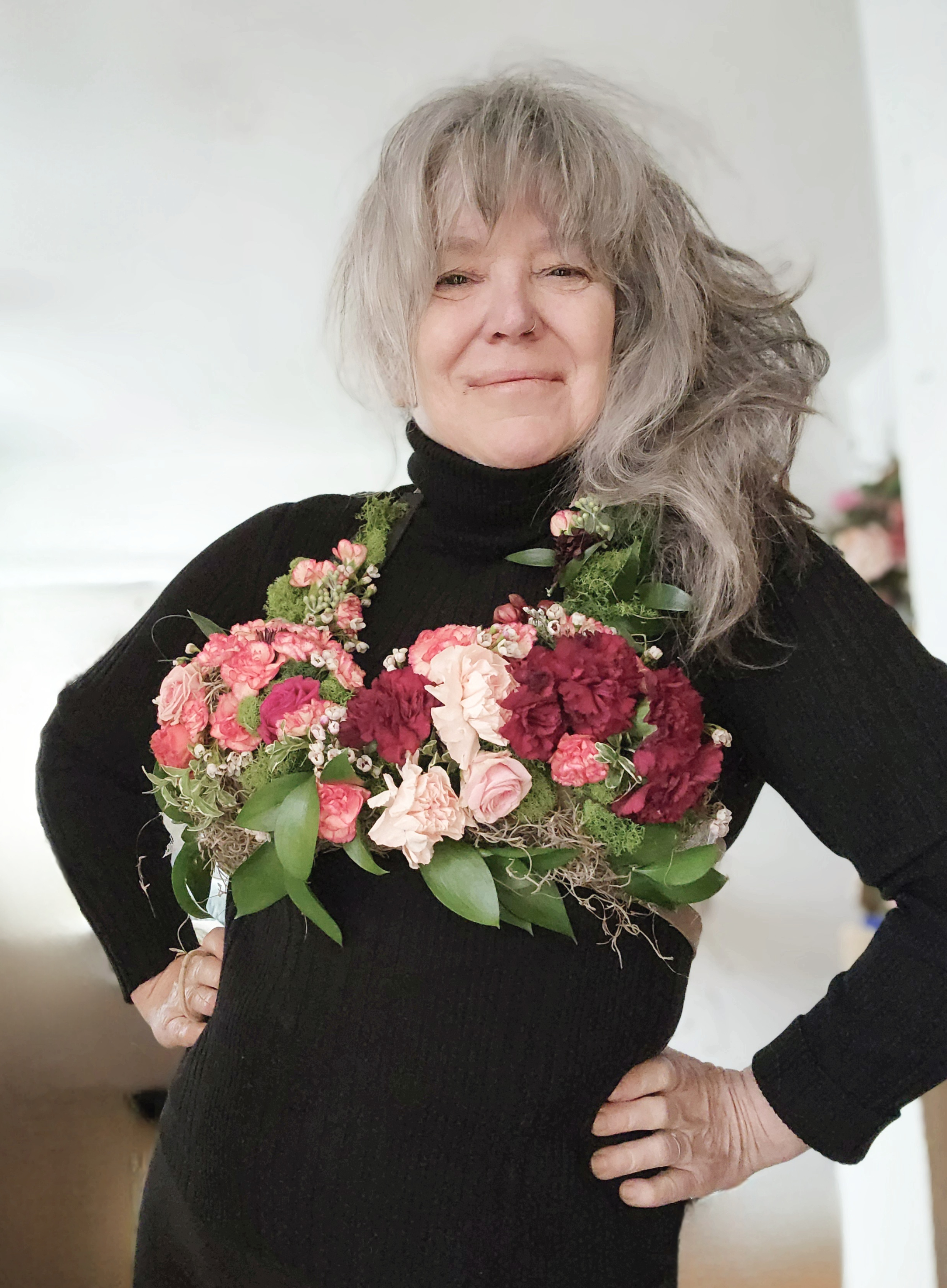 Middle aged white female wearing a dark turtleneck and bright floral bra.